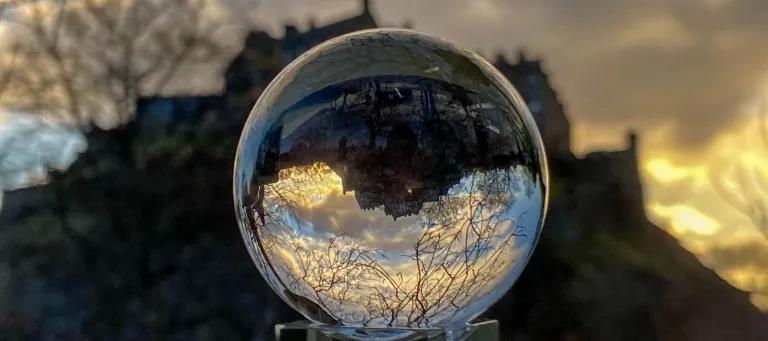Image of glass ball in front of Edinburgh Castle which sits in the background as the sun sets
